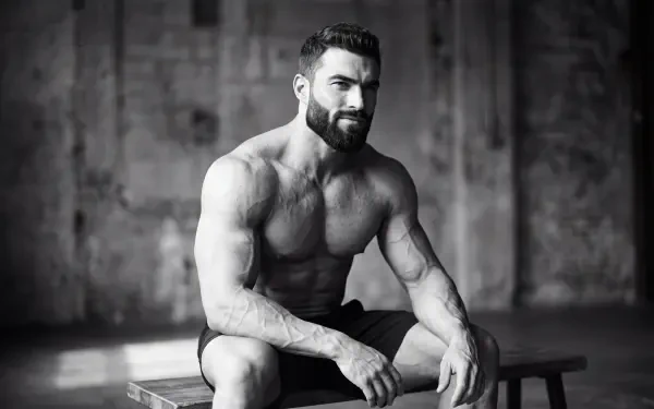 Black-and-white giga chad fitness portrait of a muscular bearded man seated on a bench, 5K Ultra HD PC desktop wallpaper and background.