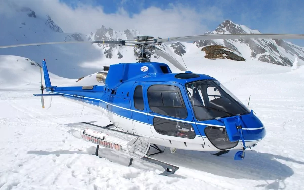 A blue helicopter rests on a snowy landscape, set against a backdrop of majestic mountains. This HD image serves as a striking desktop wallpaper and background.
