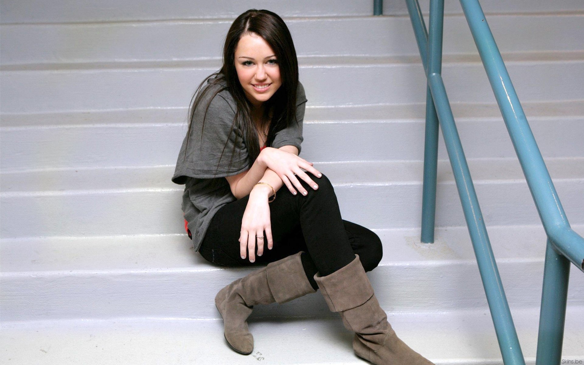 HD PC desktop wallpaper of a young female musician seated on indoor stairs in a casual outfit and boots — music-themed background featuring a pop artist vibe.