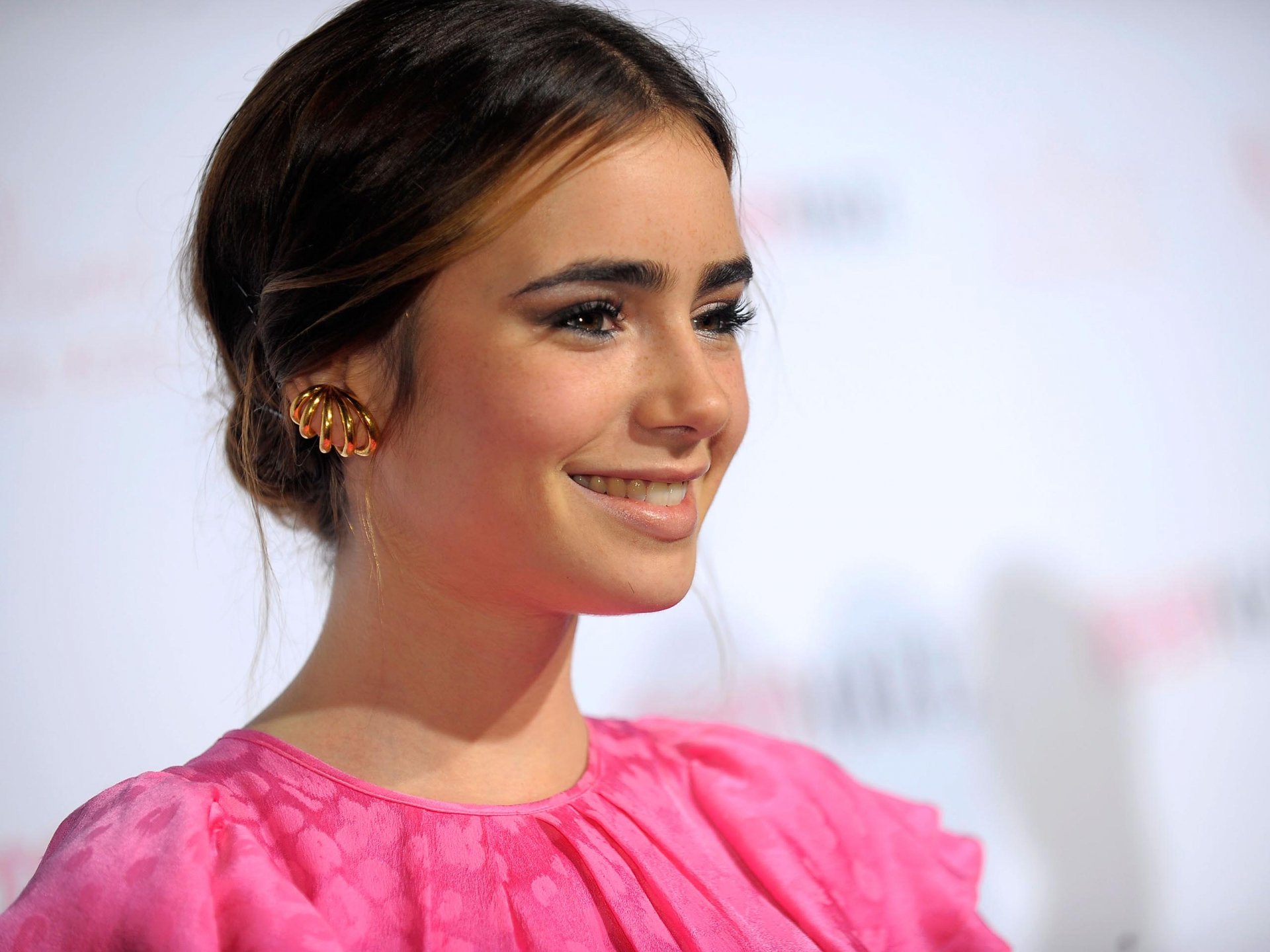 Lily Collins smiles brightly in a vibrant pink dress, showcasing her elegant style in this HD PC desktop wallpaper. A captivating image of the celebrated actress.