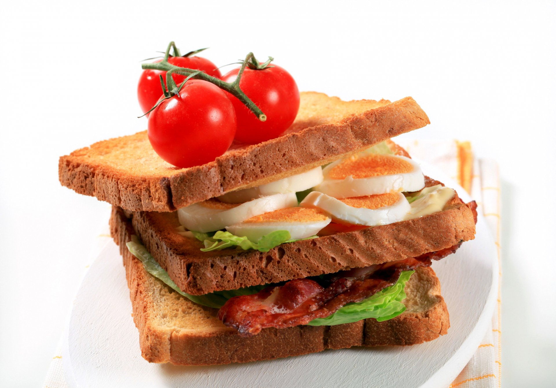 Tomato toast sandwich with lettuce, egg slices and bacon on stacked toasted bread, vivid food close-up — high-resolution 2K Quad HD PC desktop wallpaper and background.