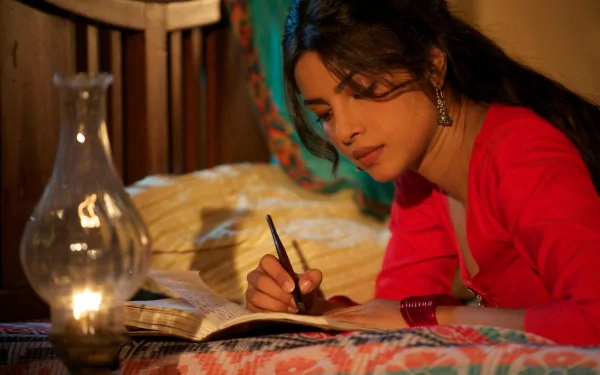 A captivating HD wallpaper featuring Priyanka Chopra, elegantly dressed in red, writing in a notebook by lantern light, set against a cozy, warmly lit backdrop.