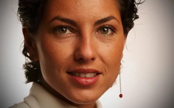Close-up of a woman with short, curly hair and a subtle smile, featuring green eyes and a red earring. This HD image serves as a striking desktop wallpaper and background.