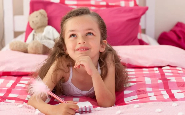 A cheerful child lying on a pink bed, writing in a notebook with a fluffy pen, captured in 4K Ultra HD photography as a vibrant desktop wallpaper.