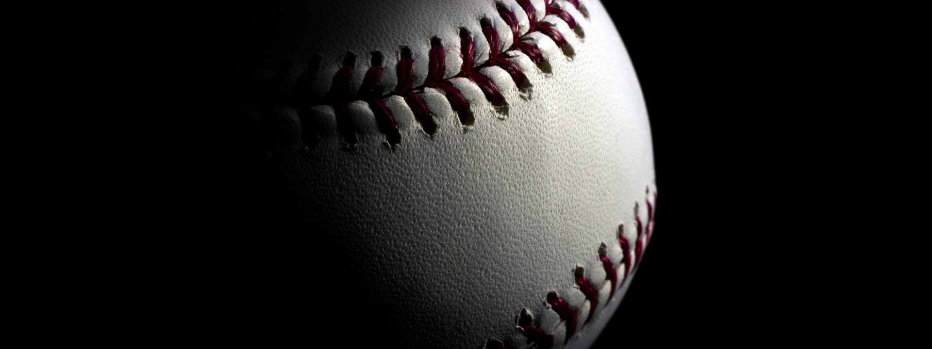 Close-up HD desktop wallpaper of a white baseball with red stitching, highlighting its texture and detail against a dark background in a sports-themed image.