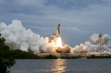 HD desktop wallpaper showing a space shuttle vehicle launching with flames and smoke against a partly cloudy sky over water.