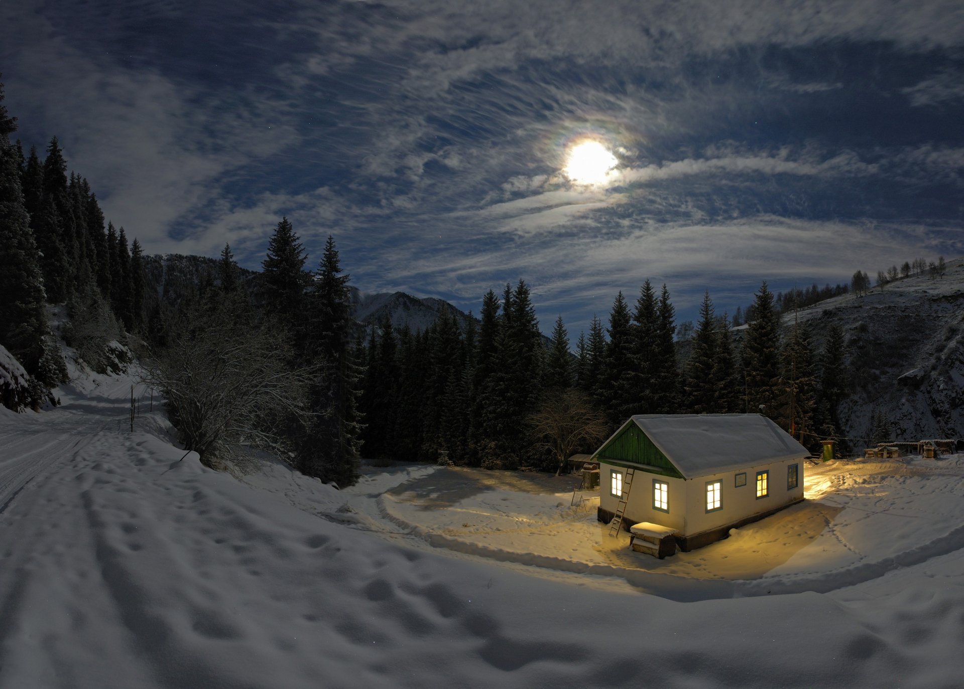 A warmly lit house nestled in a snowy winter landscape under a glowing full moon, captured in stunning 4K Ultra HD photography.
