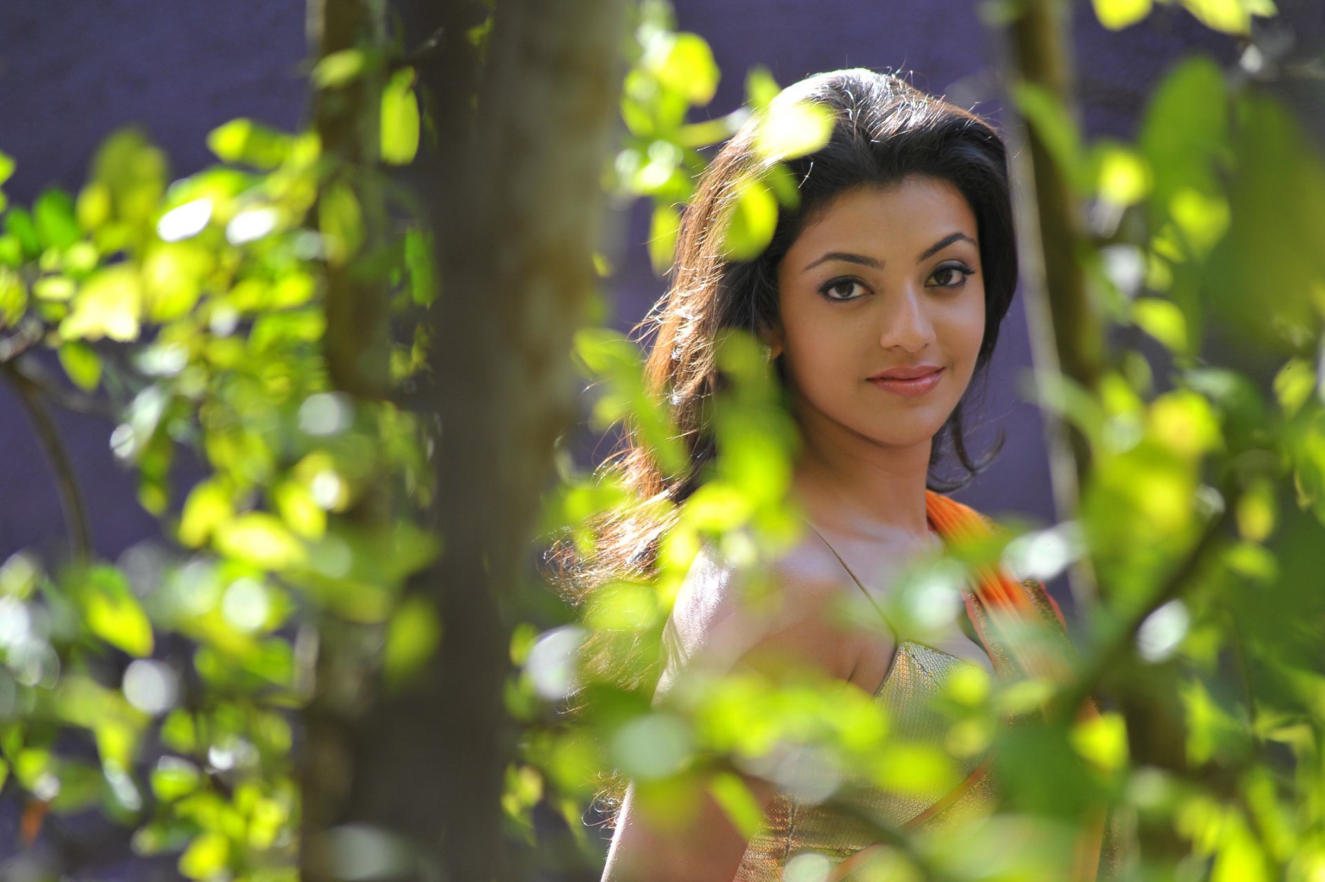 A stunning HD desktop wallpaper featuring celebrity Kajal Aggarwal surrounded by lush greenery, capturing her graceful beauty and vibrant expression.