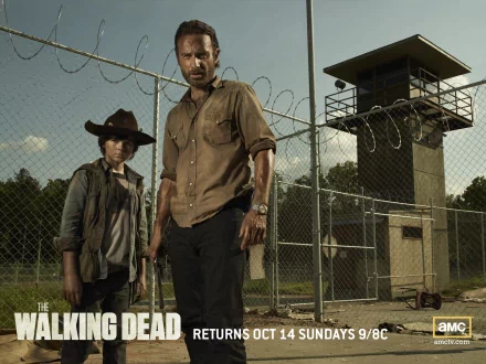 Rick Grimes and Carl Grimes stand outside a prison fence in a promotional image for the horror TV show The Walking Dead. The image features actors Andrew Lincoln and Chandler Riggs.