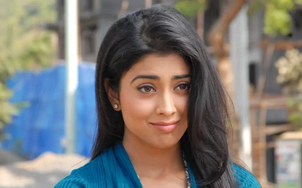 A vibrant HD desktop wallpaper featuring Shriya Saran, showcasing her charismatic smile and confident demeanor against a blurred background.