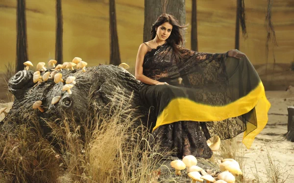 HD PC desktop wallpaper featuring celebrity Genelia D'Souza in a black and yellow saree sitting on a textured log amidst dry grass and mushrooms.