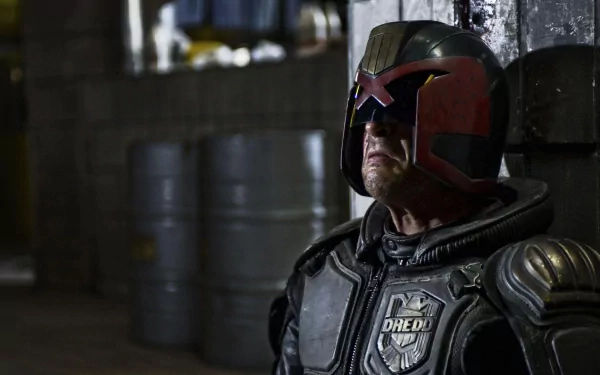 HD PC desktop wallpaper from the movie Dredd: close-up of armored Judge Dredd in helmet and visor, standing in a dim industrial corridor with stacked barrels.