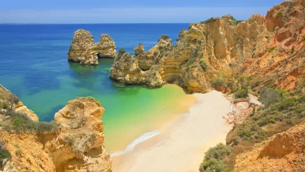 A stunning view of the coastline in Portugal, featuring golden cliffs, clear turquoise waters, and a secluded beach, showcasing the beauty of nature at the horizon.
