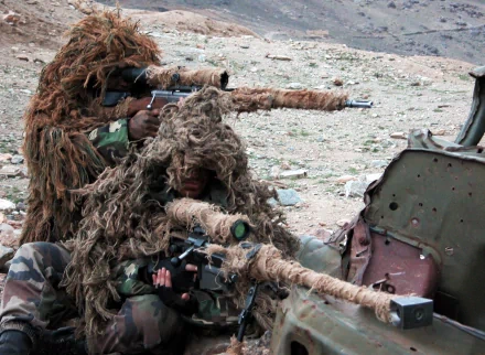 HD desktop wallpaper depicting two military snipers in ghillie suits aiming through camouflage-covered rifles in a rugged, rocky terrain.
