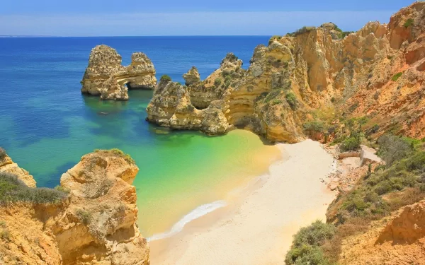 A stunning view of the coastline in Portugal, featuring golden cliffs, clear turquoise waters, and a secluded beach, showcasing the beauty of nature at the horizon.