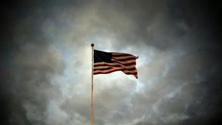 Man-made American flag on a pole waving against a dramatic cloudy sky, HD PC desktop wallpaper background.