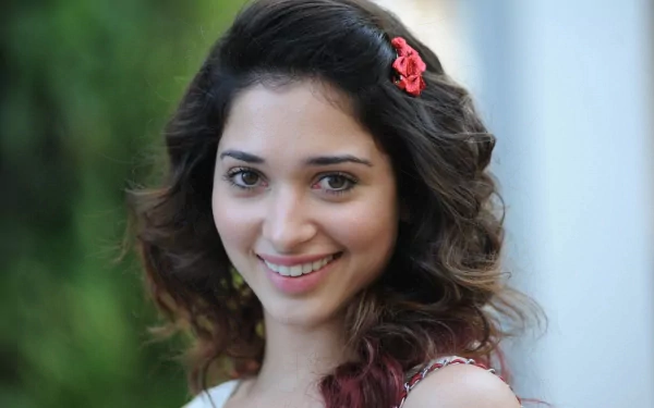 HD PC desktop wallpaper featuring celebrity Tamannaah Bhatia smiling with soft curls and a red hair clip against a blurred light background.