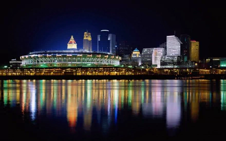 Night view of Cincinnati's illuminated skyline in Ohio, including a stadium and city buildings, reflected vividly on the calm water surface.