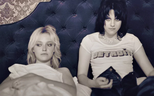 HD desktop wallpaper featuring Kristen Stewart and Dakota Fanning from the movie The Runaways, set against a dark tufted headboard background.