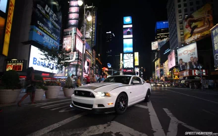 A Ford Mustang stands prominently in the bustling streets of Times Square at night, illuminated by vibrant billboards and city lights, showcasing urban energy and style.