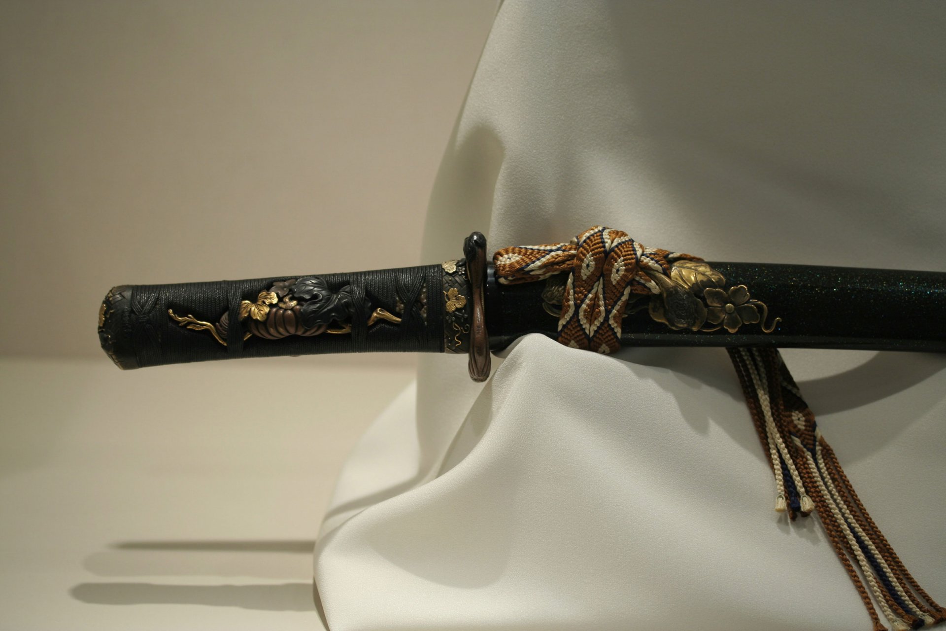 A detailed close-up of a beautifully crafted sword handle, featuring intricate designs, set against a softly draped fabric background. An elegant HD desktop wallpaper choice.