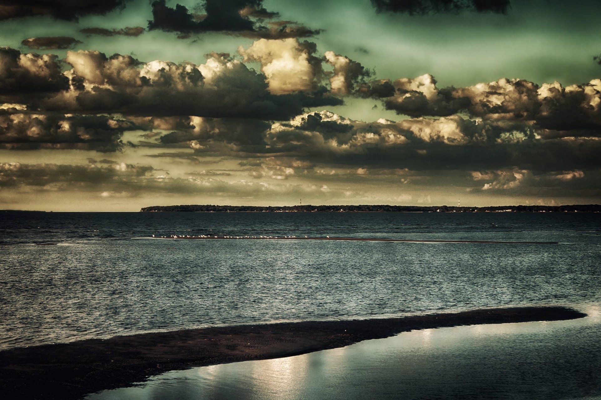 HD PC desktop wallpaper background — dramatic cloud-filled sky over calm coastal water with a curved sandbar, moody green-tinted tones.