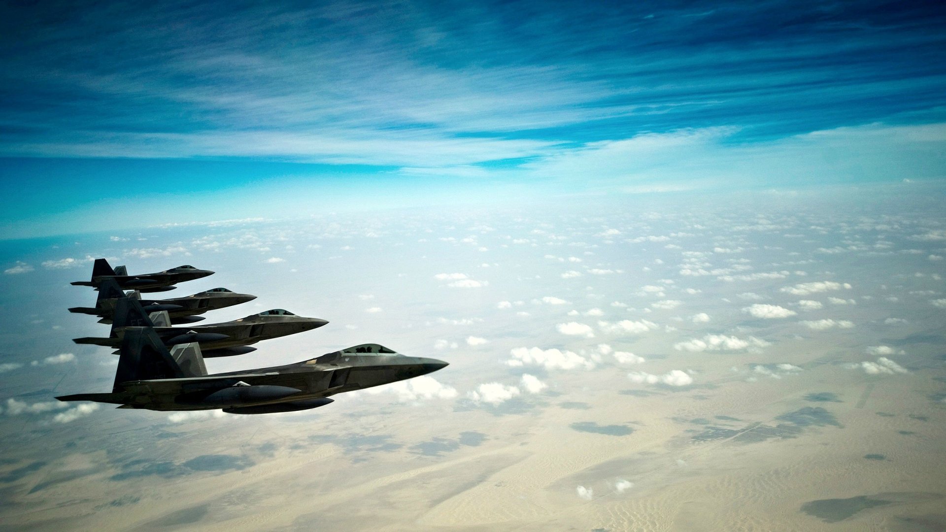 A striking HD wallpaper of military Lockheed Martin F-22 Raptors soaring through a clear sky, showcasing their sleek design against a backdrop of clouds and vast terrain.