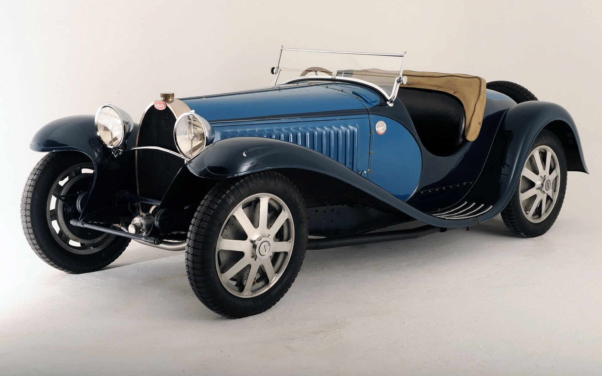 HD desktop wallpaper showing a classic Bugatti vehicle with blue and black bodywork and vintage design elements against a plain background.