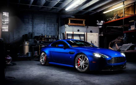 HD PC desktop wallpaper featuring a sleek blue Aston Martin parked inside an industrial garage with dramatic lighting highlighting its design.