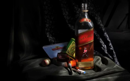 HD desktop wallpaper featuring a bottle of whisky alongside a cigar, matchstick, and tobacco pouch arranged on dark fabric with moody lighting.