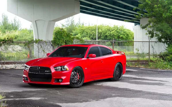 Red Dodge Charger parked beneath an overpass, wet pavement and chain-link fence in the background — high-detail 4K Ultra HD PC desktop wallpaper.