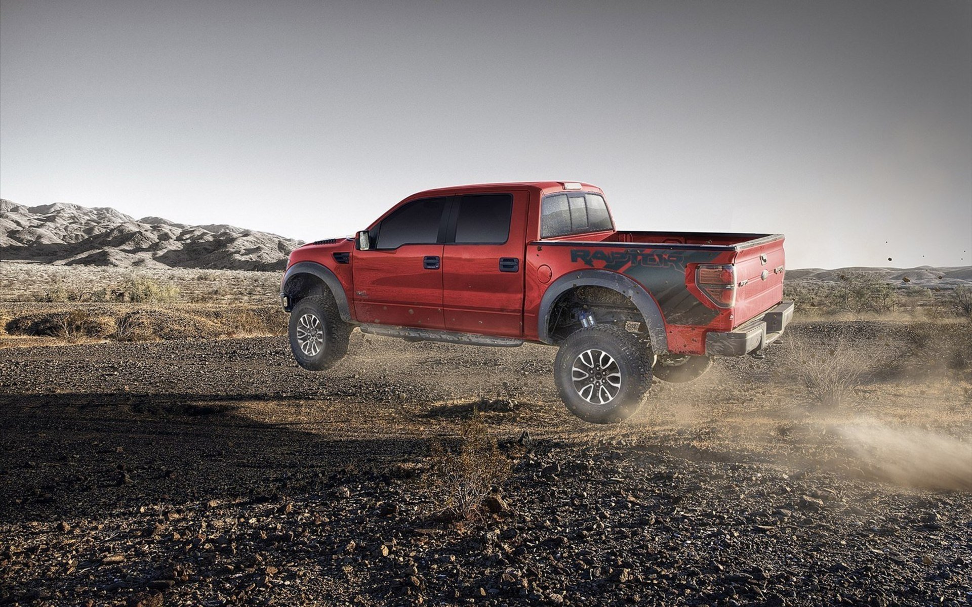 A red Ford Raptor truck kicking up dust on a rugged desert landscape, captured in high definition for a PC desktop wallpaper and background.