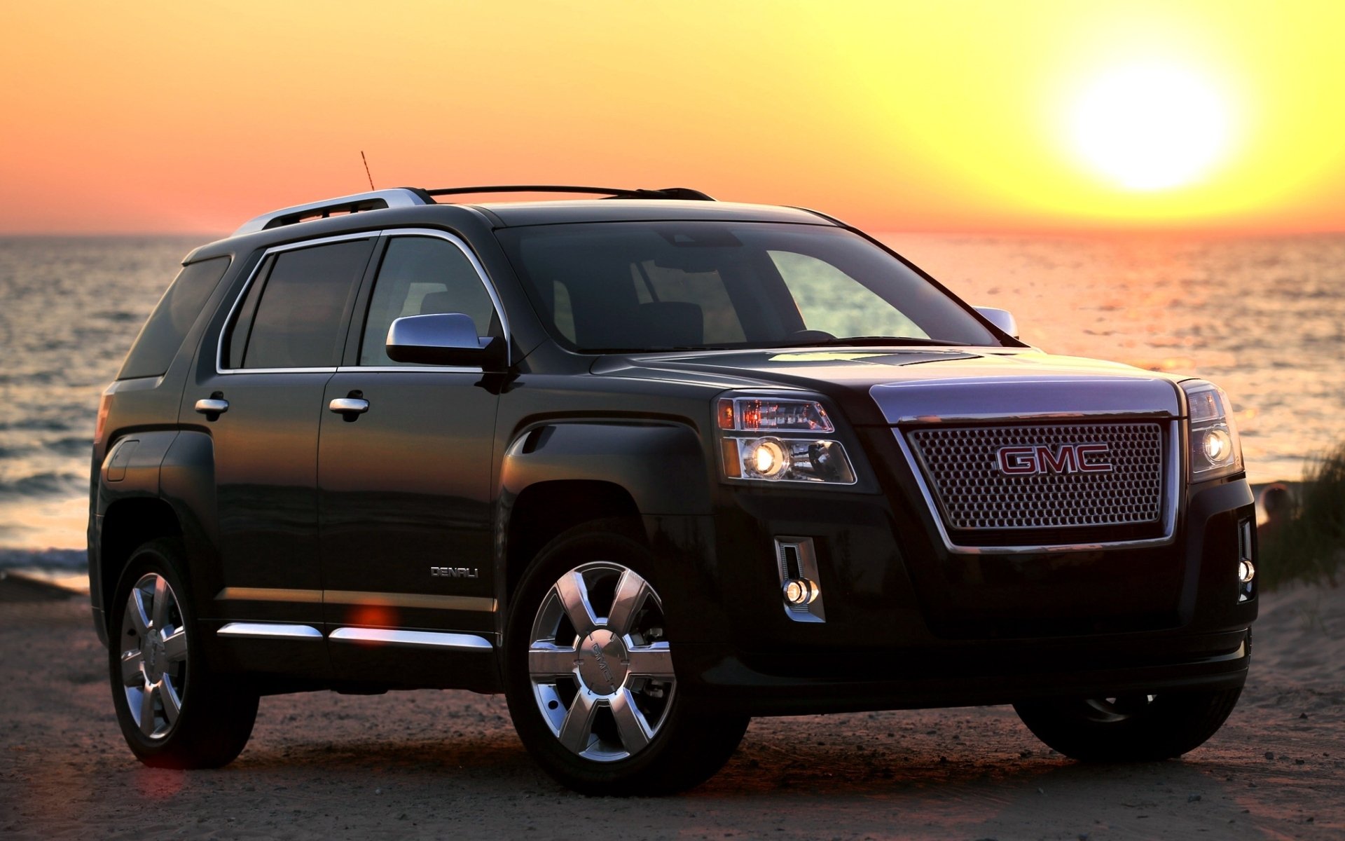 Black GMC SUV parked on a beach at sunset, its silhouette and chrome gleaming on the sand — HD PC desktop wallpaper and background.