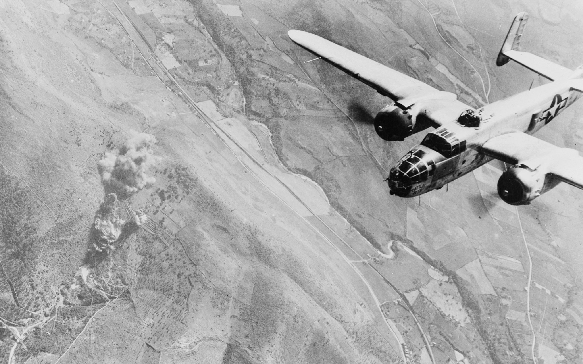 Black and white HD desktop wallpaper featuring a North American B-25 Mitchell military aircraft flying over rugged terrain.