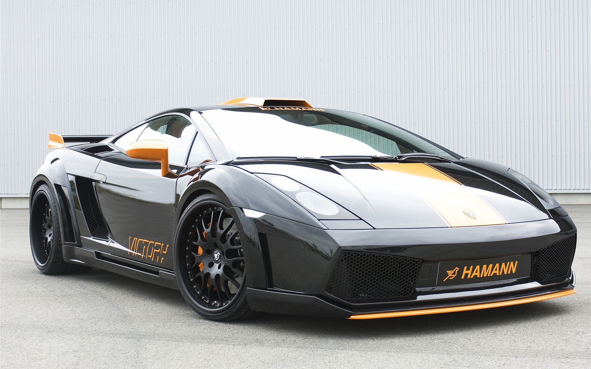 HD PC desktop wallpaper of a Hamann-tuned Lamborghini Gallardo vehicle in black and orange with widebody stance, low profile and sporty details against a light industrial backdrop.