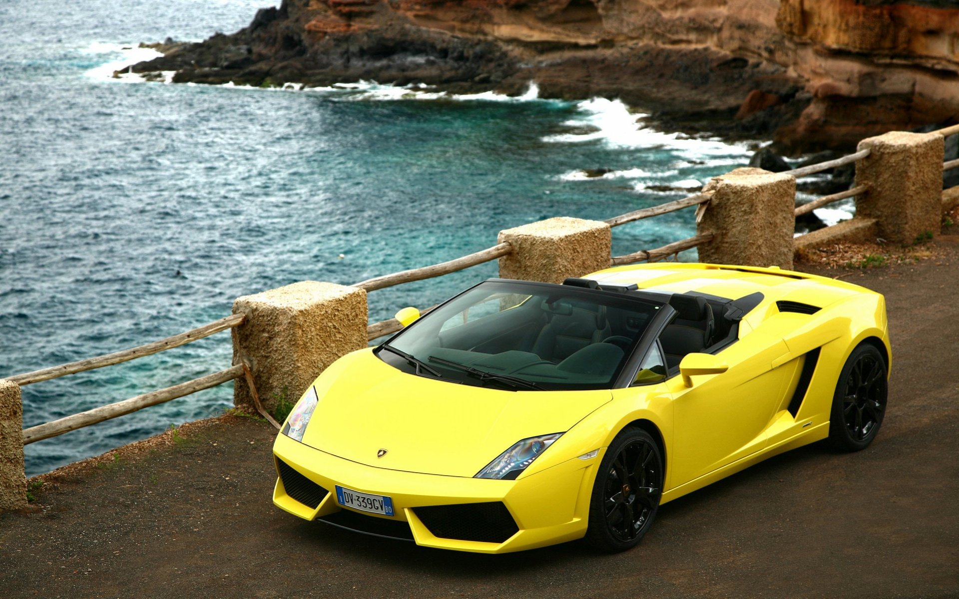 Yellow Lamborghini Gallardo convertible vehicle parked on a coastal road by cliffs and surf — 2K Quad HD PC desktop wallpaper/background.