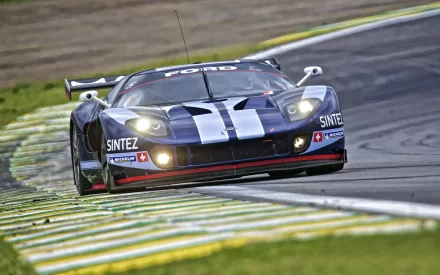 HD PC desktop wallpaper/background showing a Ford GT40 race vehicle speeding through a corner on a racetrack, low-angle shot with motion blur, black with white stripes and sponsor decals.