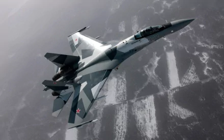 A high-definition wallpaper featuring a Sukhoi Su-27 aircraft in flight, showcasing its distinctive design and military capabilities against a backdrop of clouded terrain.