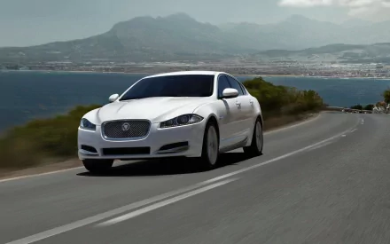White Jaguar sedan cruising a coastal highway with mountains and sea beyond — HD PC desktop wallpaper and background