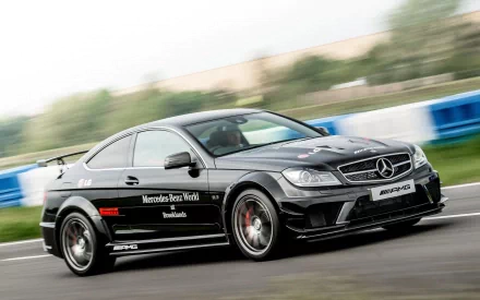 HD PC desktop wallpaper showing a black Mercedes AMG coupe racing on a track, motion-blurred background with visible sponsor decals.