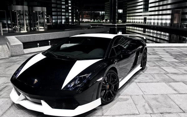 HD PC desktop wallpaper/background showing a black-and-white Lamborghini Gallardo vehicle parked on a tiled urban plaza at night with reflective modern buildings.