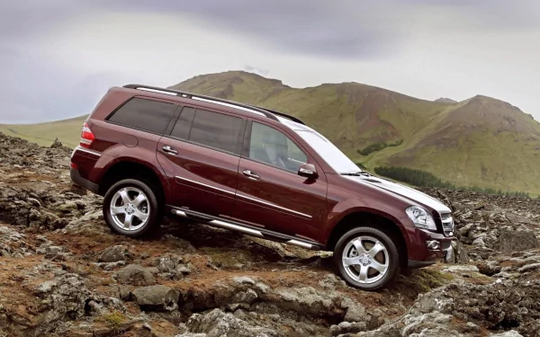 HD desktop wallpaper featuring a maroon Mercedes SUV navigating rocky terrain with hills in the background.