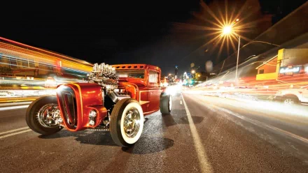 HD PC desktop wallpaper showcasing a vibrant red hot rod vehicle on a city street at night with dynamic light trails and a glowing streetlamp.