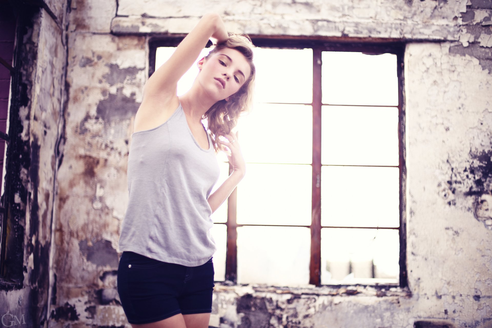 Young woman stretching by an industrial window in soft light against distressed walls; 2K Quad HD PC desktop wallpaper (person's name omitted for privacy).
