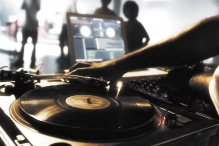 A dynamic DJ scene featuring a hand on a turntable, set against a vibrant background with silhouettes of people enjoying music, creates an engaging HD desktop wallpaper.