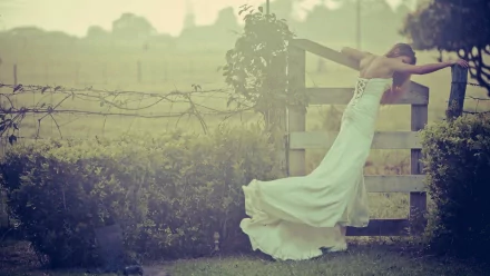 HD desktop wallpaper featuring a bride in a flowing white gown leaning on a wooden fence in a misty, serene outdoor setting.