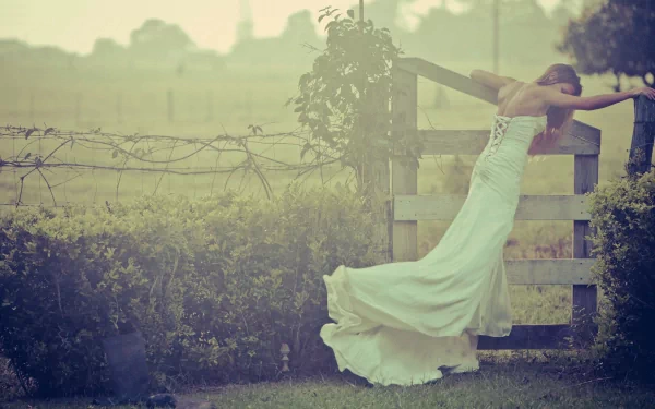 HD desktop wallpaper featuring a bride in a flowing white gown leaning on a wooden fence in a misty, serene outdoor setting.