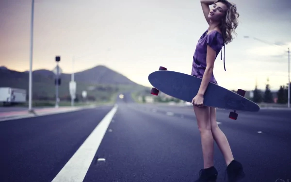 2K Quad HD PC desktop wallpaper/background: woman standing on an empty road at dusk holding a longboard, windblown hair and a relaxed pose.