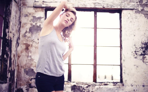 Young woman stretching by an industrial window in soft light against distressed walls; 2K Quad HD PC desktop wallpaper (person's name omitted for privacy).