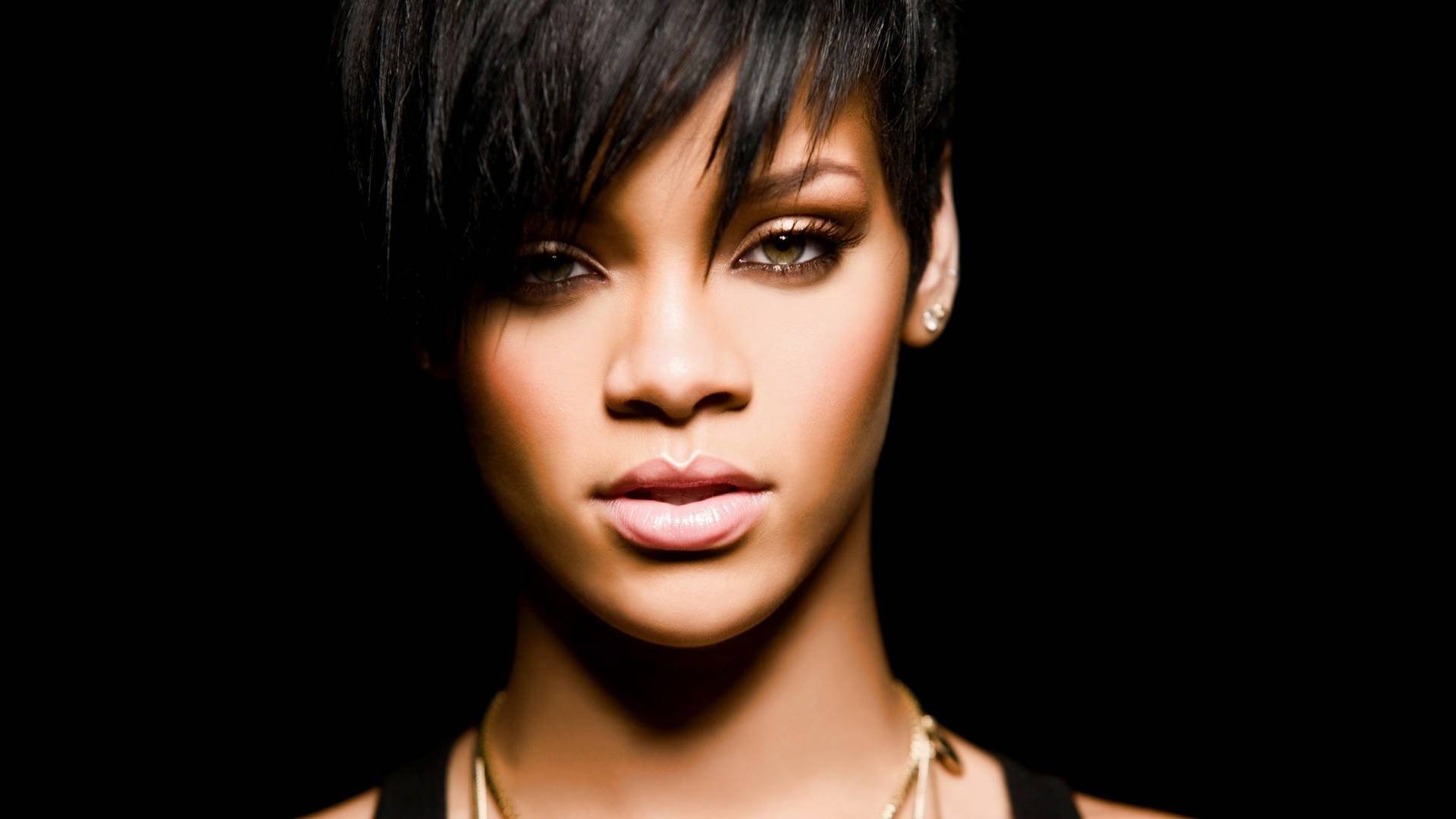 HD PC desktop wallpaper featuring a close-up portrait of Rihanna with dark background, emphasizing her striking gaze and short hairstyle in a music-themed image.